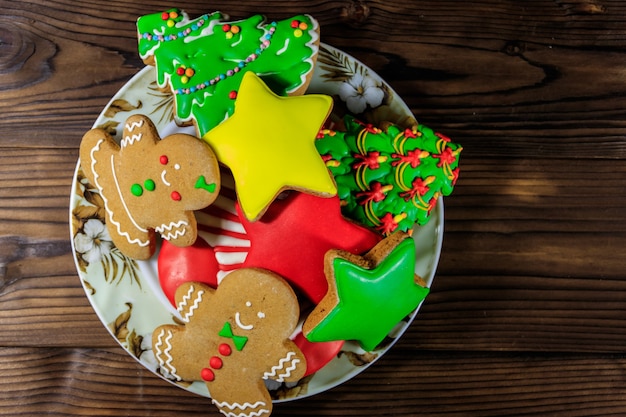 Assiette avec de délicieux biscuits de Noël festifs en pain d'épice en forme d'arbre de Noël, bonhomme en pain d'épice, étoile et bas de Noël sur table en bois. Vue de dessus