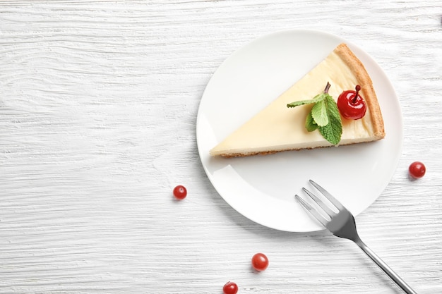 Assiette avec un délicieux cheesecake et cerise sur table blanche