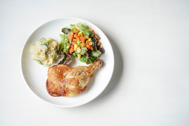 Assiette de délicieux steak de cuisses de poulet grillé aux légumes et pommes de terre à salade sur blanc