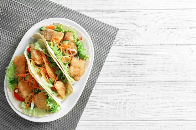 Assiette avec de délicieux tacos au poisson sur une table en bois