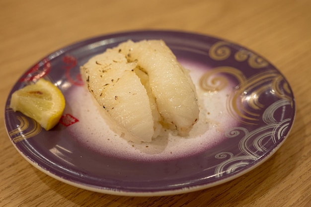 Une assiette avec deux morceaux de poisson dessus et un citron à côté.