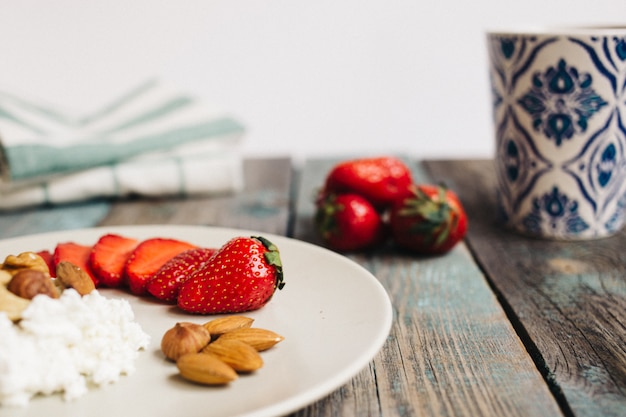 Assiette avec du fromage cottage, des fraises et des noix, une tasse de café et des serviettes sur une table en bois, des aliments sains, le petit déjeuner