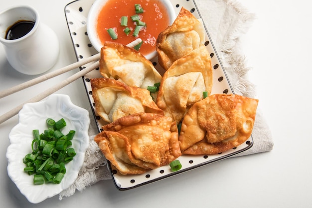 Une assiette d'empanadas frites avec des oignons verts et un bol de sauce.