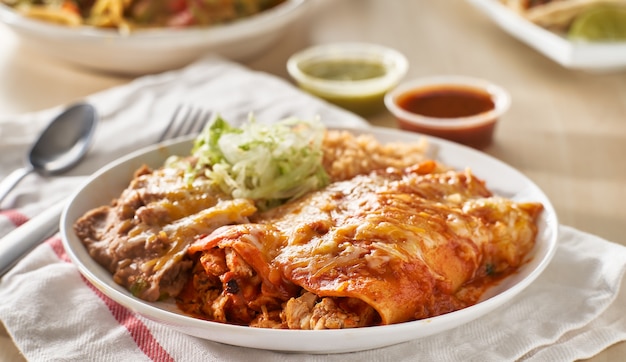 Photo assiette d'enchilada mexicaine avec sauce rouge, haricots frits et riz