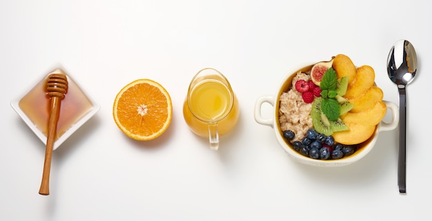 Assiette avec de la farine d'avoine et des fruits, une demi-orange mûre et du jus fraîchement pressé dans une carafe en verre transparent, du miel dans un bol sur une table blanche. Petit-déjeuner sain