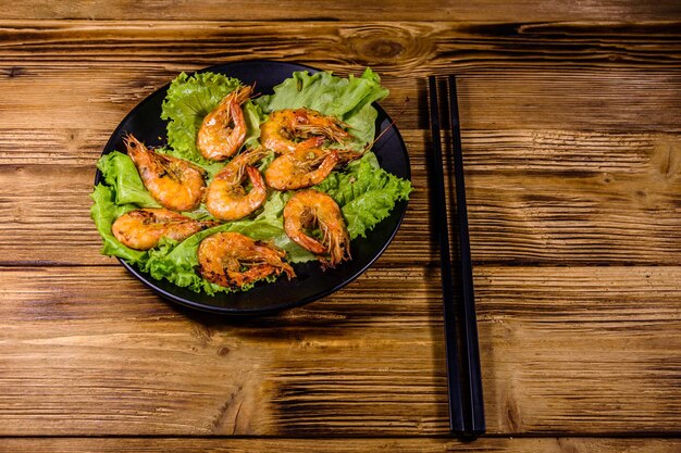 Assiette avec des feuilles de laitue de crevettes grillées et des baguettes sur une table en bois
