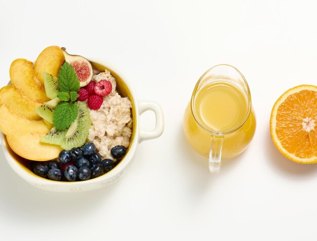 Une assiette avec des flocons d'avoine et des fruits une demi-orange mûre et du jus fraîchement pressé dans une carafe en verre transparent sur un tableau blanc