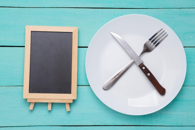 Assiette avec fourchette et couteau mini tableau de craie vide sur fond de bois bleu Menu du restaurant Espace de copie