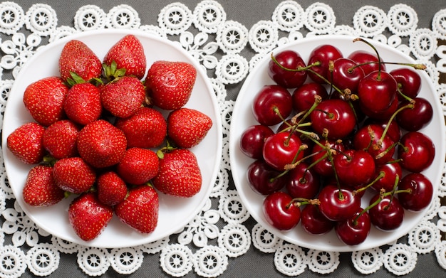 Assiette de fraises et une assiette de cerises rouges sur une serviette en dentelle, vue de dessus