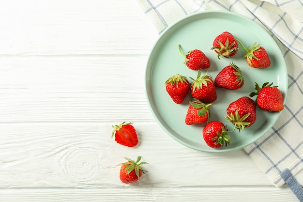 Assiette avec des fraises fraîches et un torchon sur fond en bois blanc, vue de dessus et espace pour le texte