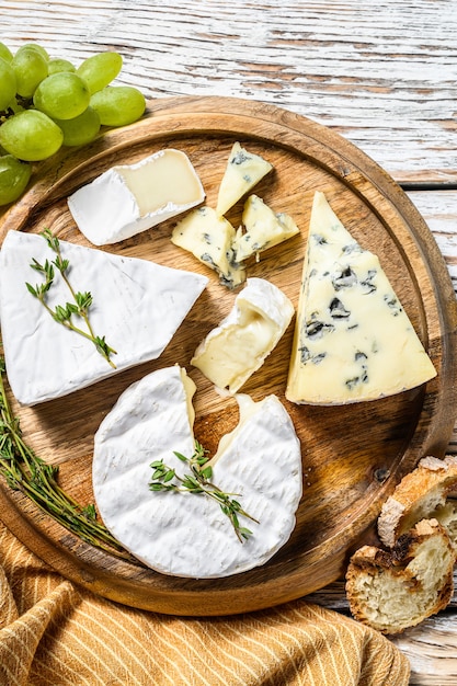 Assiette de fromages au camembert, brie et fromage bleu aux raisins. Fond en bois blanc. Vue de dessus.