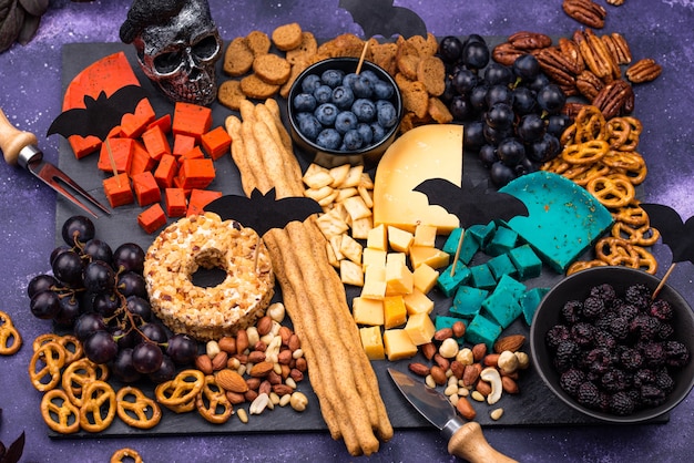 Photo assiette de fromages avec des baies, des raisins, des noix et des collations. nourriture d'halloween.