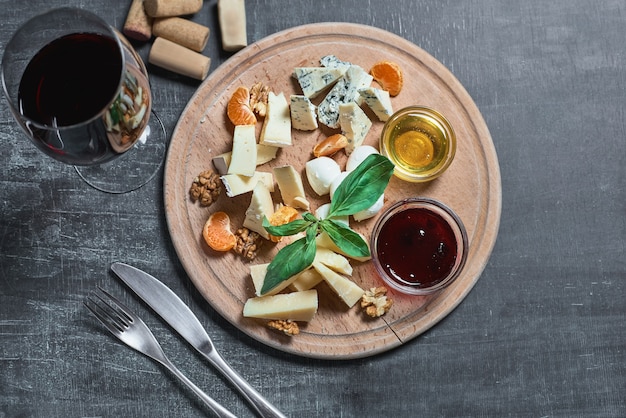 Assiette de fromages délicieux apéritif pour le vin - fromage, miel, noix, confiture, servi sur une planche en bois légère et un verre de vin rouge sur une surface en bois