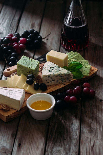 Assiette de fromages sur fond sombre. Brie, bleu doré, gouda, raisins, noix, vin