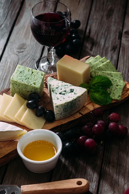 Assiette de fromages sur fond sombre. Brie, bleu doré, gouda, raisins, noix, vin