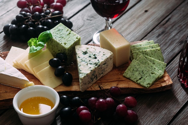 Assiette de fromages sur fond sombre. Brie, bleu doré, gouda, raisins, noix, vin