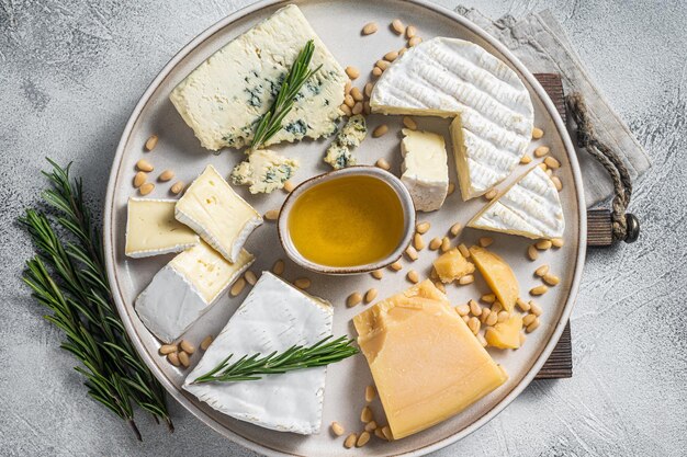Assiette de fromages français avec camembert, brie, gorgonzola, parmesan, miel, noix et herbes. Fond blanc. Vue de dessus.