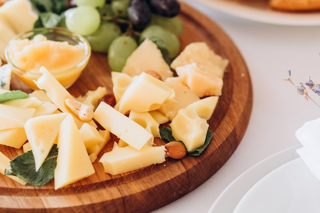 Assiette de fromages avec une grappe de raisin, du miel et des noix. Gouda, parmesan, mozzarella, gorgonzola sur une planche de bois.