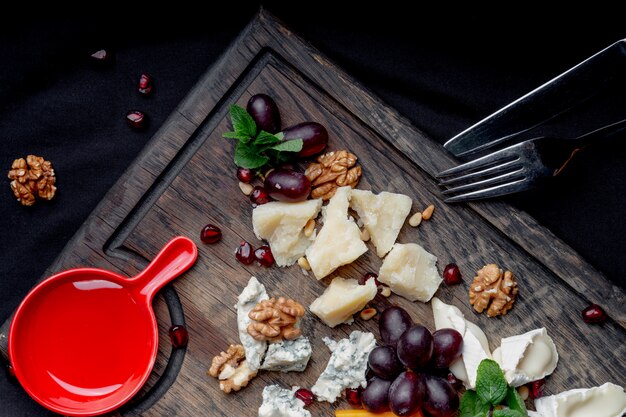 Assiette de fromages servi avec des raisins et des noix sur un fond en bois