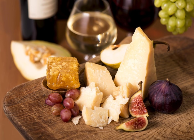 Assiette de fromages servie avec des craquelins de figues de melon de raisins et de vin blanc sur une table en bois