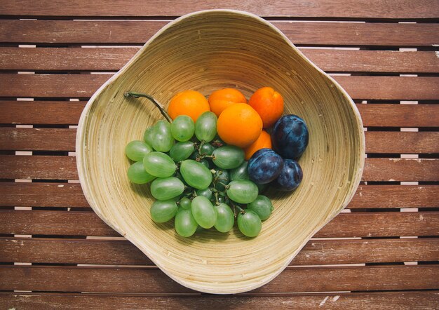 Assiette avec des fruits frais mélangés sur le fond en bois. Assortiment de fruits juteux sur table en bois