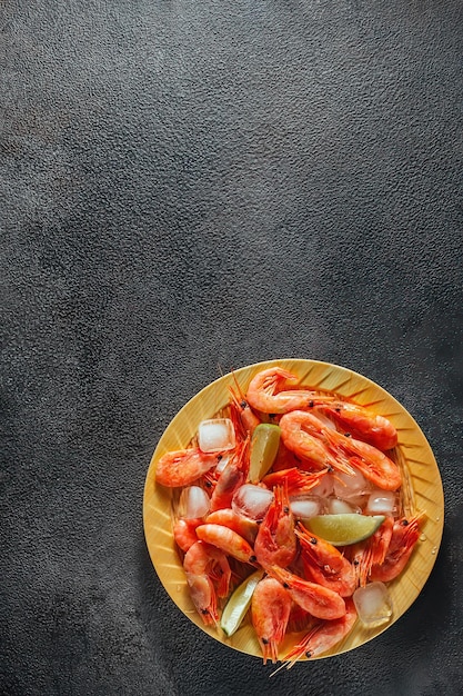 Assiette de fruits de mer de crevettes crues et de glace, avec des tranches de citron vert sur fond sombre, à plat