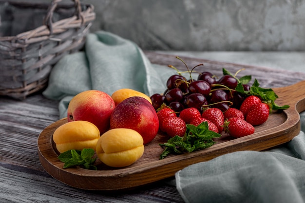 Assiette de fruits sains, fraises, pommes, pêches, abricots sur une table en bois gris foncé, vue de dessus, gros plan, mise au point sélective.