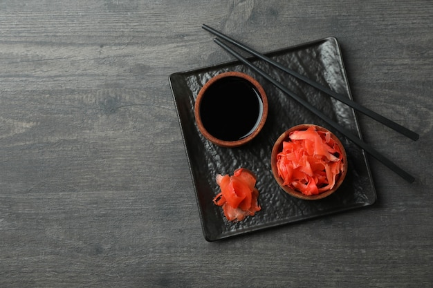 Assiette avec gingembre mariné, sauce soja et baguettes sur une surface en bois sombre