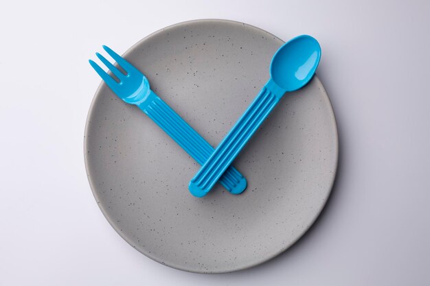 Assiette grise d'horloge avec une cuillère et une fourchette en plastique concept de repas de temps de repas