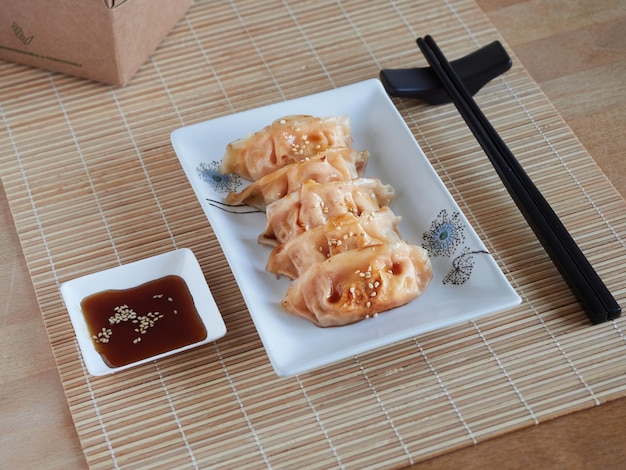 Assiette de gyozas servi avec sauce soja et graines de sésame avec des baguettes sur une nappe en bambou