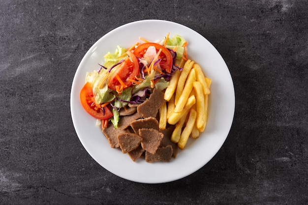 Assiette de kebab, légumes et frites sur fond de pierre noire