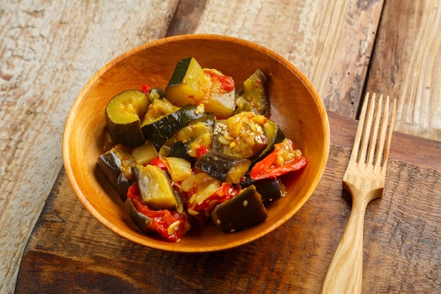 Une assiette de légumes grillés sur une planche de bois à côté d'une fourchette en bois