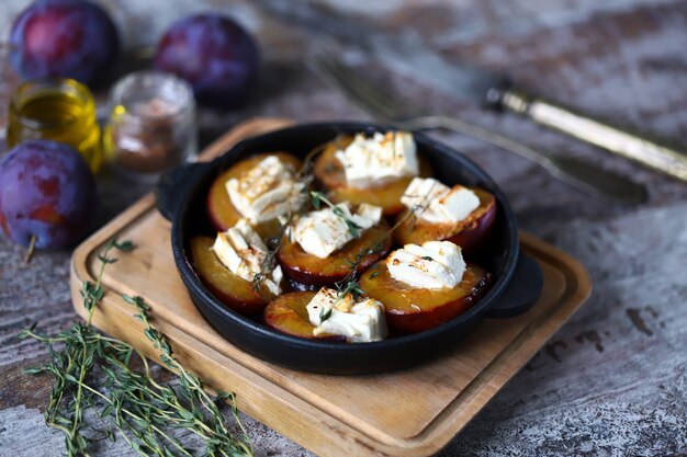 Assiette avec des moitiés de prune cuites au four avec du fromage feta et des herbes sur une surface en bois minable