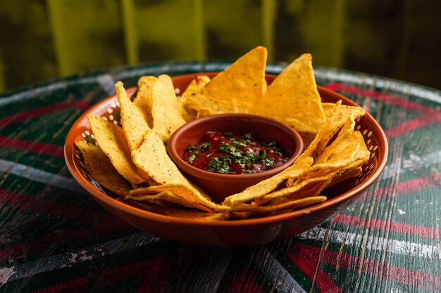 Une assiette de nachos avec trempette de salsa épicée sur une table en bois