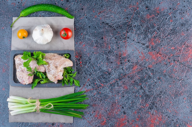 Assiette noire d'ailes de poulet crues sur une surface en marbre.