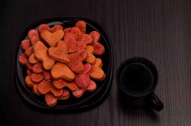 Assiette noire avec des biscuits en forme de coeur rouges et une tasse de thé sur un tableau noir, Saint-Valentin. Vue de dessus