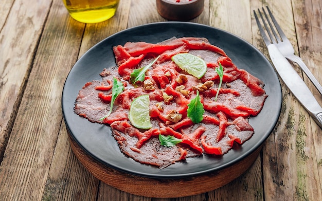 Assiette noire avec carpaccio de boeuf avec bébé roquette et citron vert sur fond de bois rustique Mise au point sélective