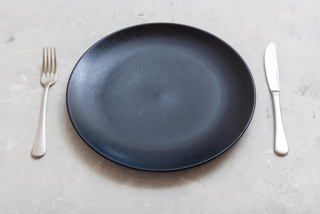 Assiette noire avec cuillère à couteau sur béton gris