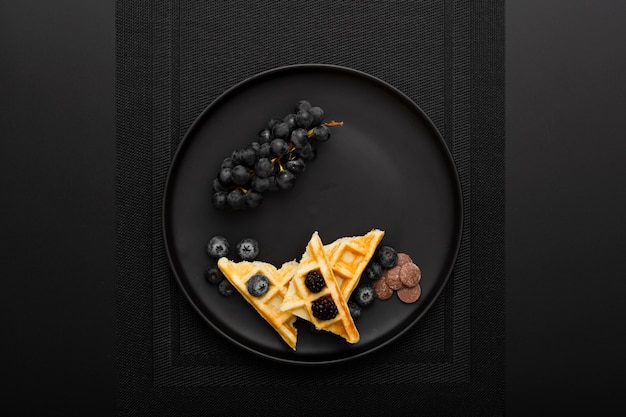 Photo assiette noire avec des gaufres et des raisins sur un chiffon foncé