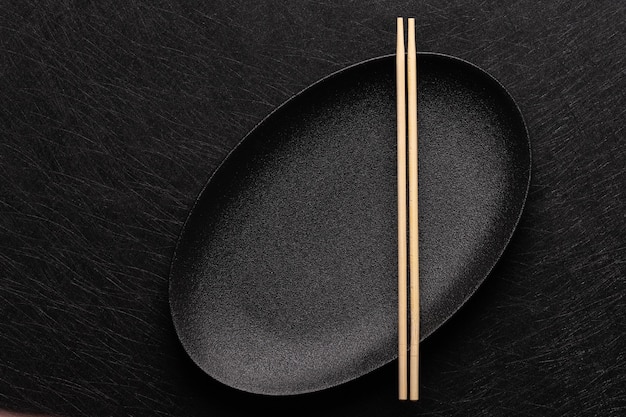 Assiette noire ovale vide avec des baguettes sur fond sombre style de cuisine japonaise vue de dessus à plat