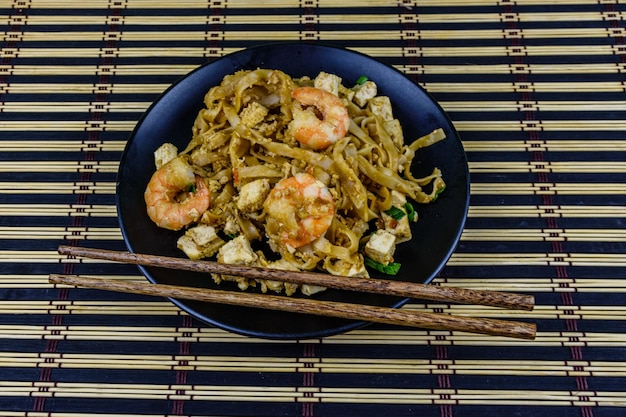 Assiette noire avec pad thai et baguettes sur une natte de bambou Vue de dessus