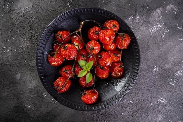 Assiette noire avec tomates confites sur fond sombre.