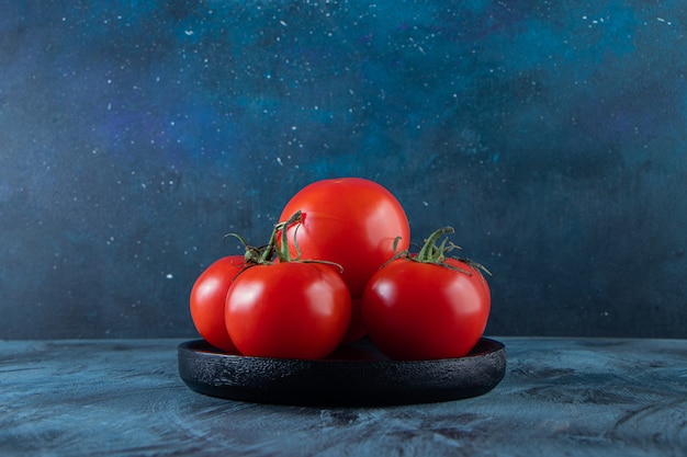 Assiette noire de tomates fraîches rouges sur mur bleu.
