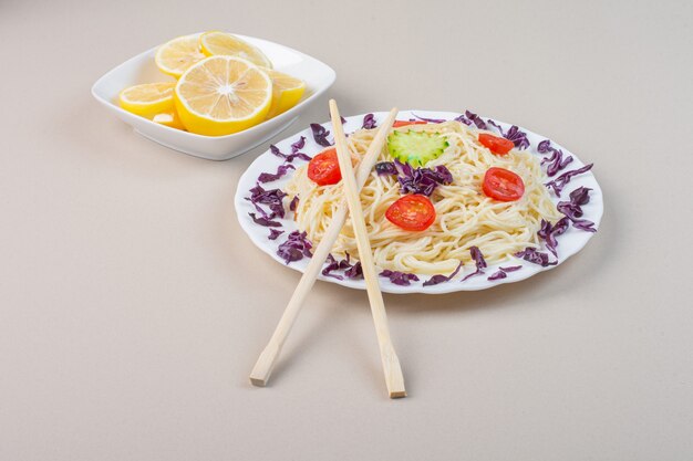 Une assiette de nouilles cuites avec des légumes et des tranches de citron frais.