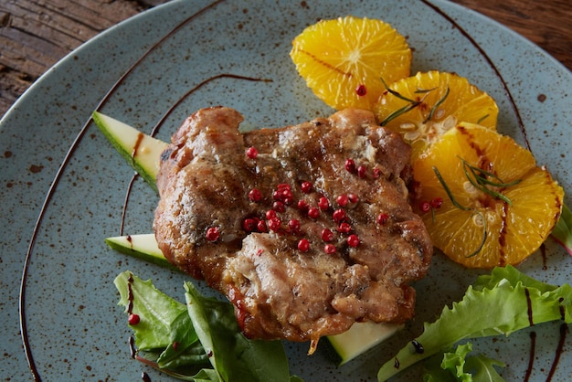 Une assiette de nourriture avec un morceau de viande et des oranges dessus.