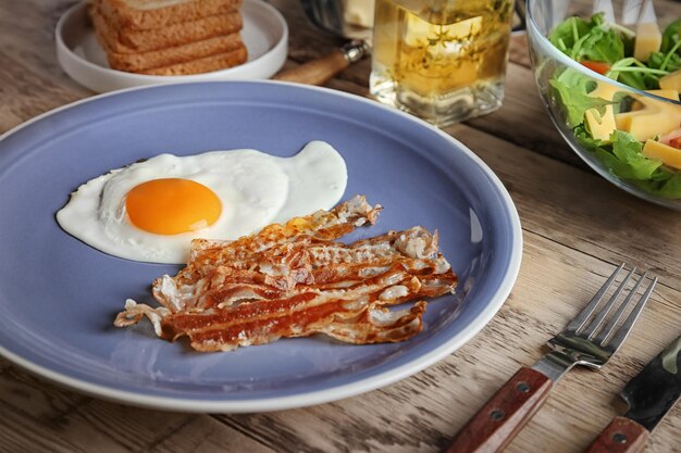 Assiette avec oeuf au plat et bacon sur table en bois