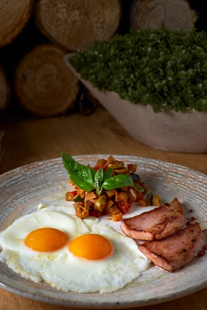 Assiette d'oeufs au plat avec bacon et légumes sur une table en bois. Petit déjeuner anglais sur table