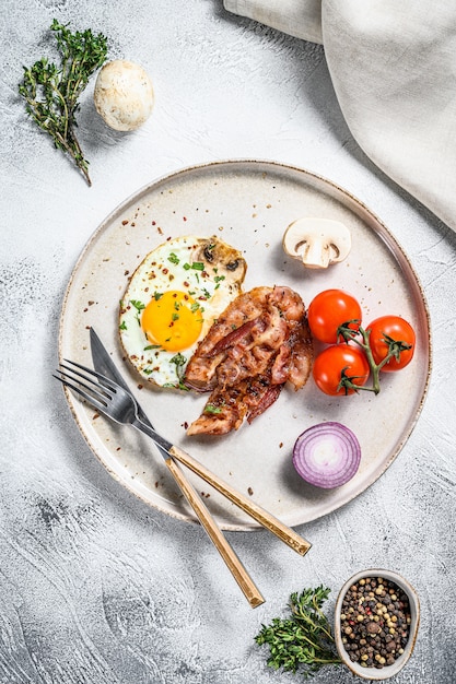 Assiette d'oeufs au plat avec bacon et tomate fraîche, champignon sur tableau blanc.