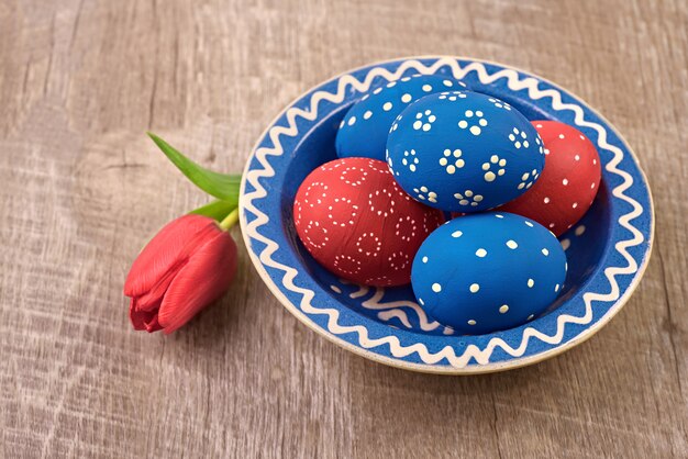 Assiette avec des oeufs de Pâques bleu et rouge et fleur de tulipe sur table en bois