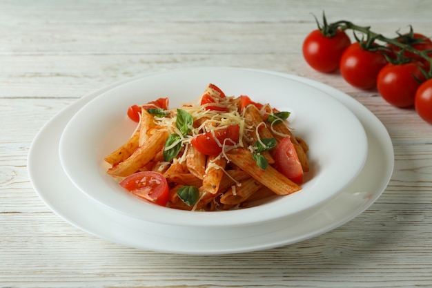 Assiette avec des pâtes à la sauce tomate et tomates sur table en bois blanc